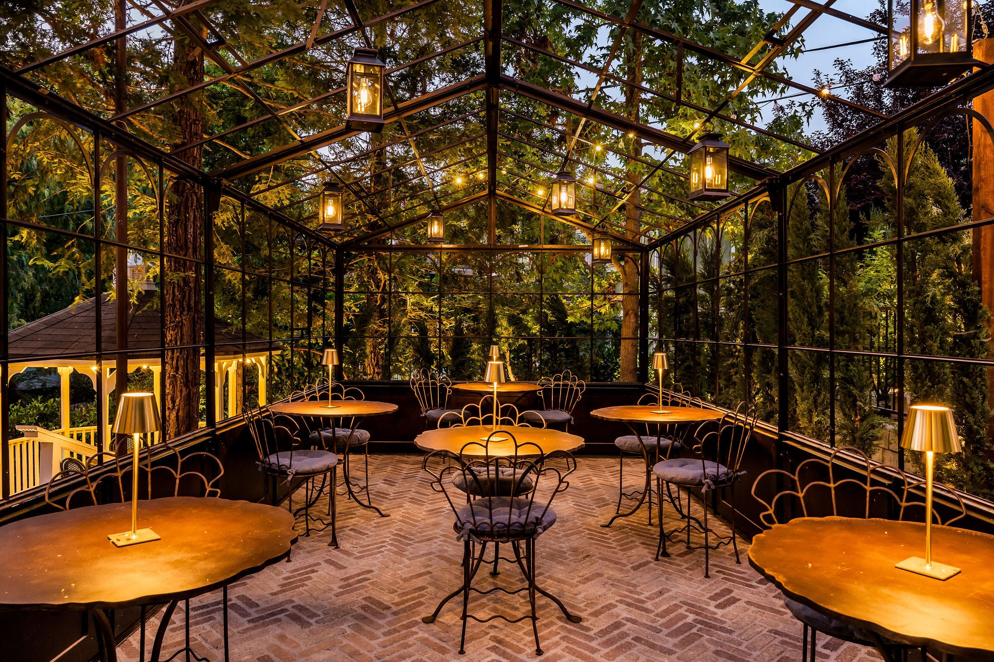 The iron and glass Wine Garden conservatory lit by lanterns at dusk