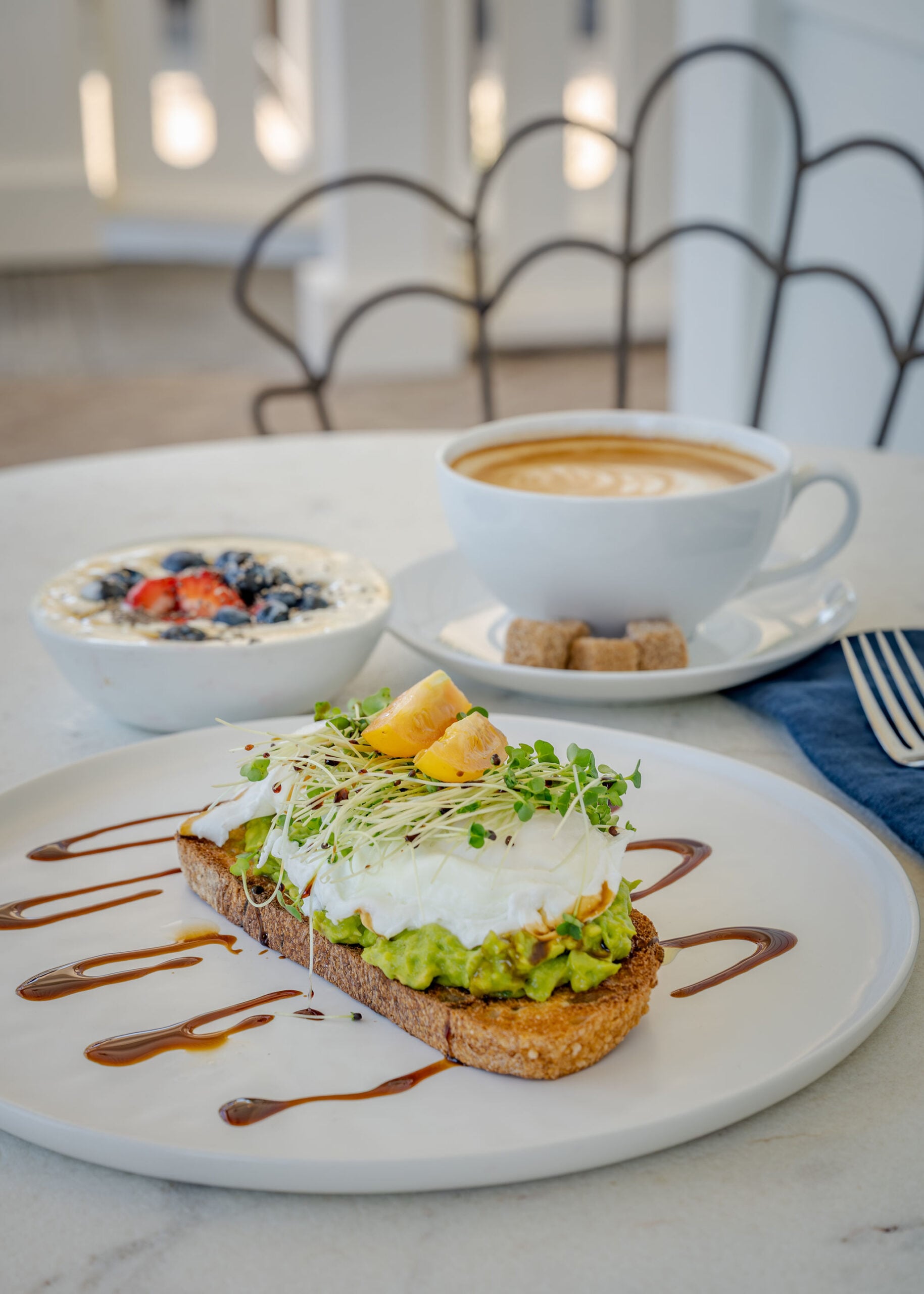 Avocado toast with a poached egg, a berry yogurt bowl, and a latte at breakfast at The Polo House